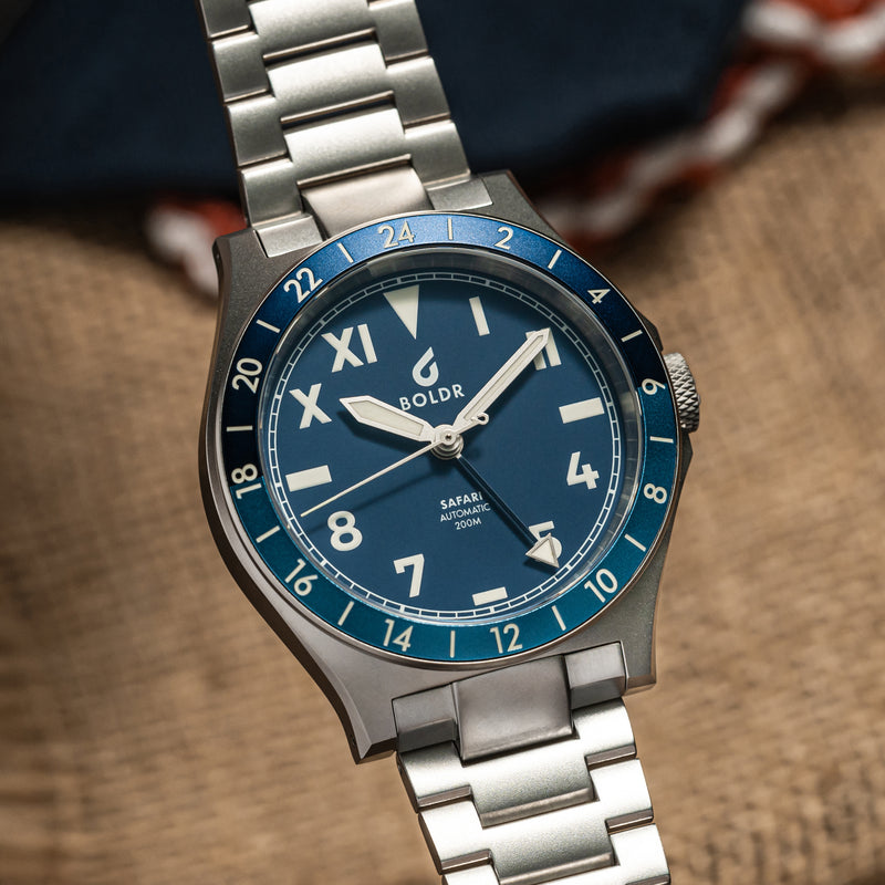 Close-up of a BOLDR Safari watch with a deep blue dial, Roman and Arabic numerals, and a stainless steel bracelet.