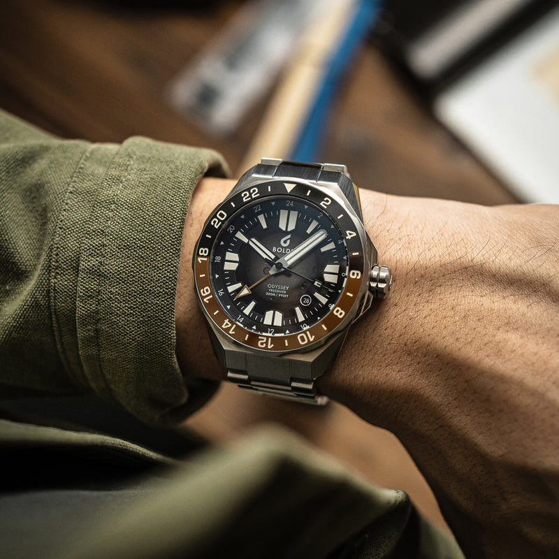 Close-up of a BOLDR automatic watch with a stainless steel bracelet and a black and chocolate brown bezel.