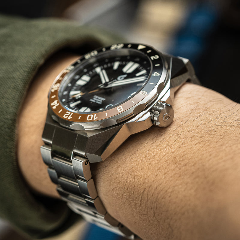 Close-up of a BOLDR automatic watch with a stainless steel bracelet and a black and chocolate brown bezel.