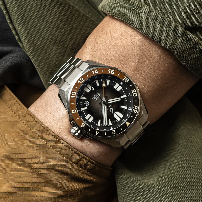 Close-up of a BOLDR automatic watch with a stainless steel bracelet and a black and chocolate brown bezel.